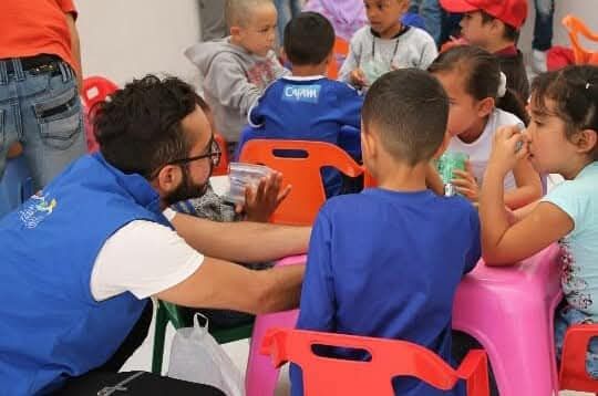 Un integrante de REDH comparte una actividad con niñas y niños sentados alrededor de una mesa